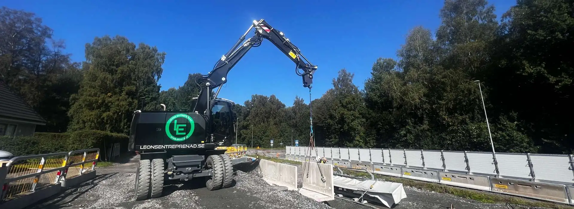 Svart hjulgrävare med Leons-logotyp lyfter betongelement vid en väg