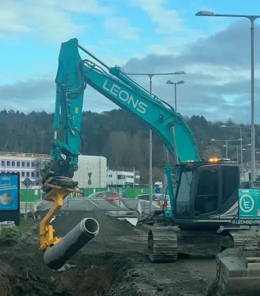 Grävmaskin med Leons-dekor som lägger ett betongrör i ett schakt