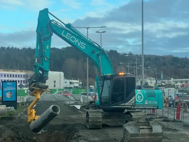 Turkos grävmaskin med Leons-dekor som lyfter ett betongrör